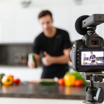 Close up of a video camera filming young smiling male blogger at the kitchen